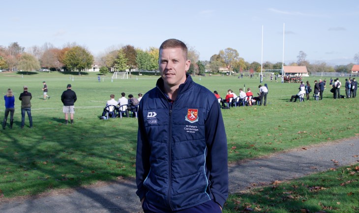 PE teacher Carl Perry standing in front of a field with a rugby game taking place. 
