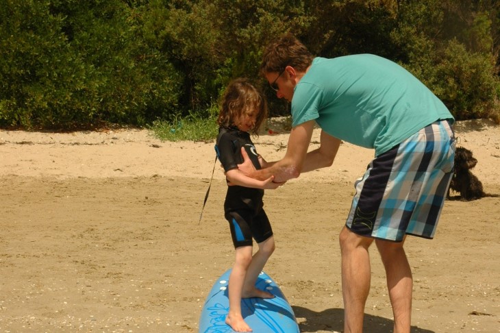 Megan's husband teaches their child to surf