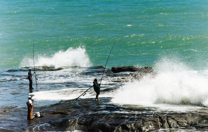 Fishers hold their rods on rocks in huge surfs