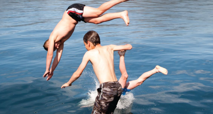 Three young boys diving into the water. 