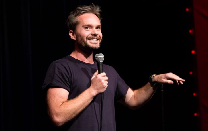 Comedian Nick Rado making a joke on stage. 