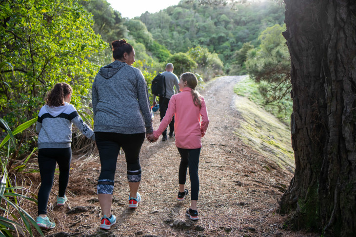 A woman walks along a forest track holding the hands of two girls