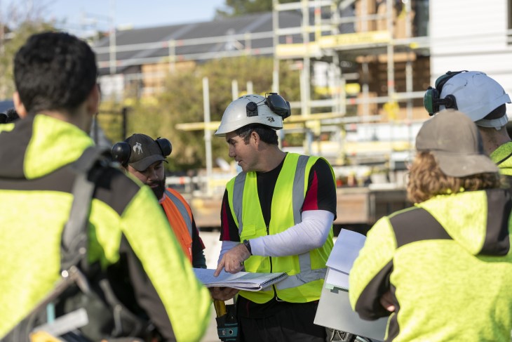 A man talking to several other construction workers in a meeting on a building site.