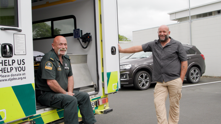 Derek leans on the back entrance of his Ambulance, with his partner Gibbo sitting on the step of the ambulance