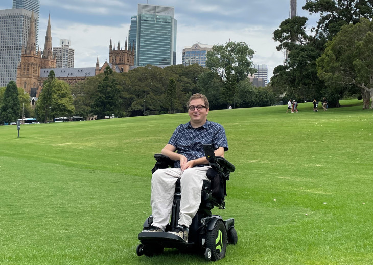 Dr Johnny Bourke sits in a wheelchair in Sydney Domain with Sydney Tower in the background