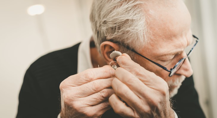 Older man inserts a hearing aid into his ear