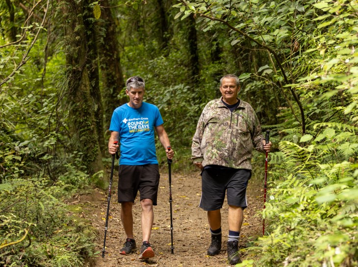 George Thompson walking in the bush with his friend Andrew Leslie, both are using walking sticks.