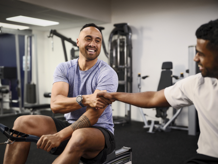 Two men sitting down and shaking hands in the gym during a work out.