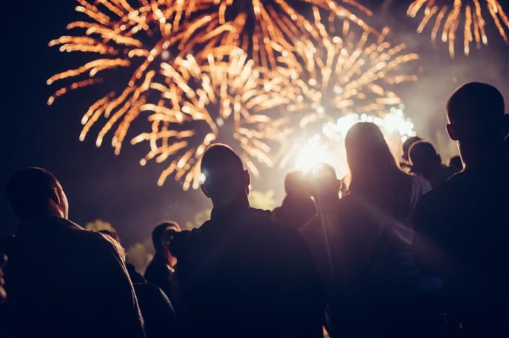 A photo showing people from behind looking up at some golden fireworks in the night sky.