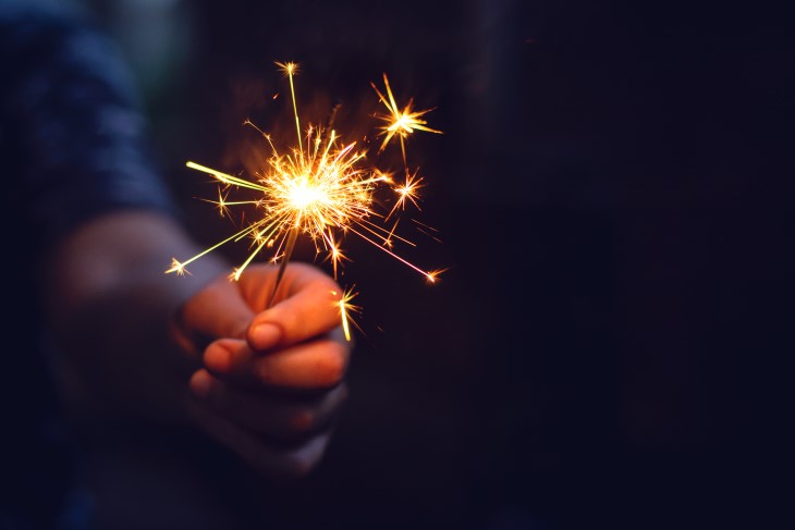 A hand holding a golden sparkler at night.