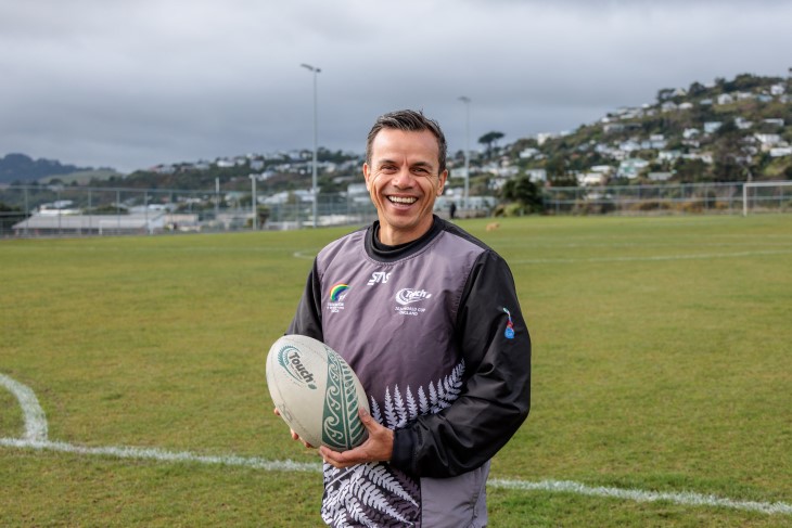 George Jahnke standing on a sports field while holding a rugby ball and smiling.