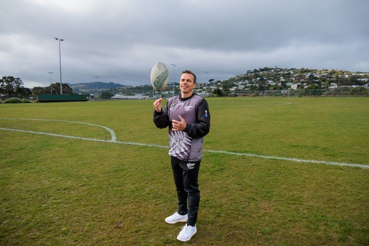 George Jahnke standing on a sports field while holding a rugby ball and smiling.