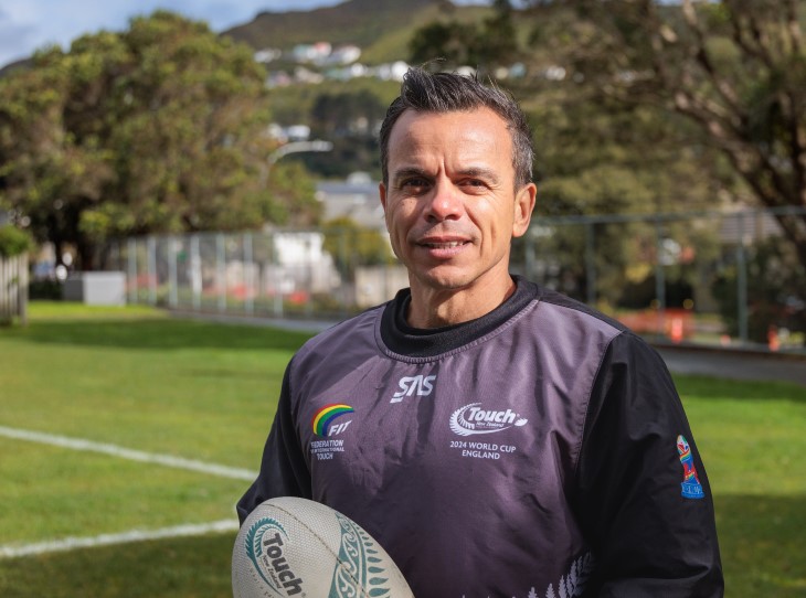 George Jahnke standing on a sports field while holding a rugby ball and smiling.