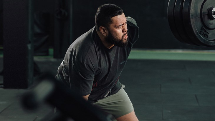 A Māori man struggles to lift a free weight in the gym.