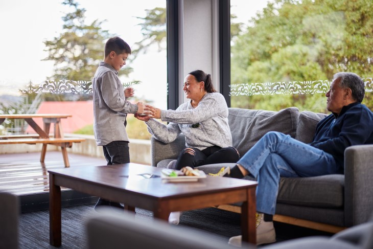 A boy giving a cup of coffee to a woman sitting on a couch as a man looks on.