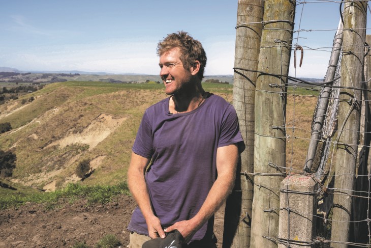 Harry Gaddum leaning on a fence post on a farm and smiling.