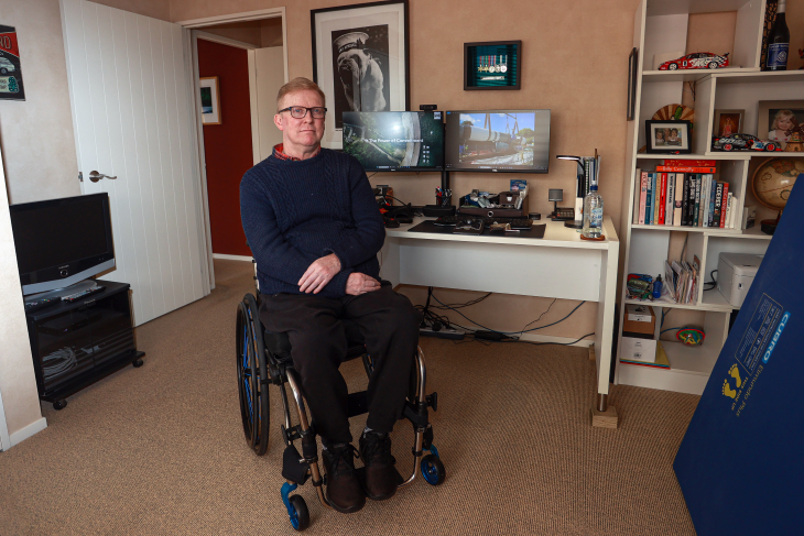 Jason Ross sitting in his home office with his work computers behind him.