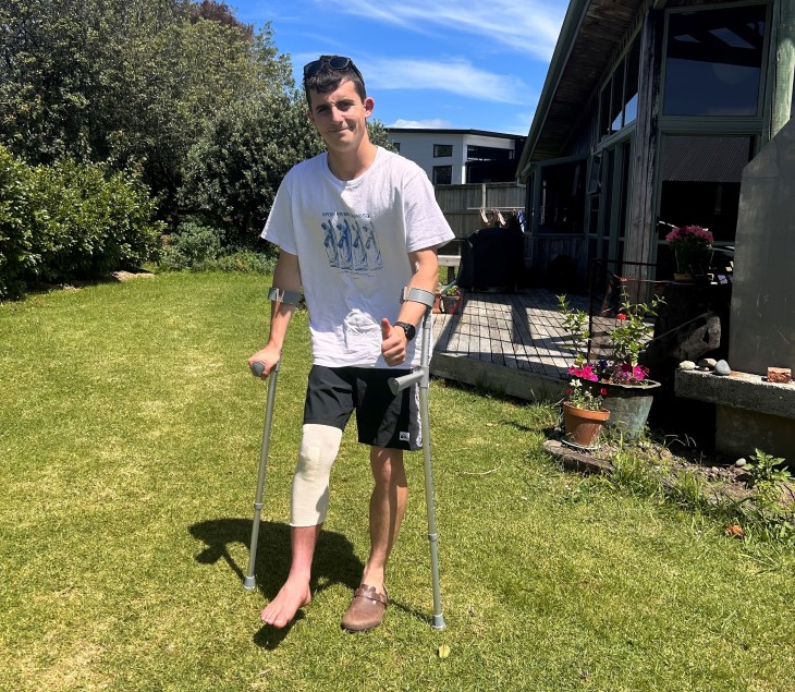 Jay Piper-Healion standing on crutches in a backyard, giving the thumbs up.