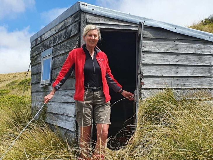 Tramper Liz Wightwick standing in front of a tramping hut. 