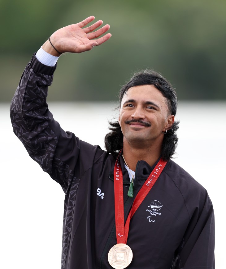 Pete Cowan raises his hand on the Paralympics podium wearing his bronze medal.