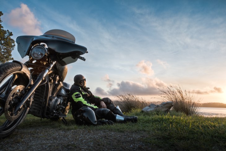 A rider sitting next to his motorbike and watching the sunset. 