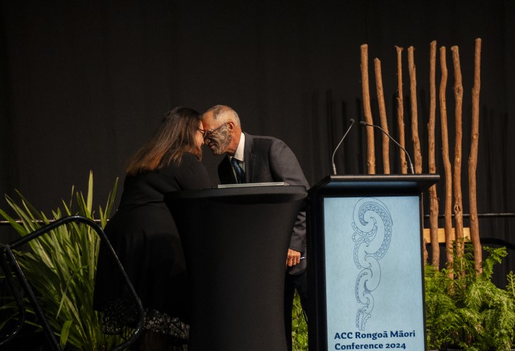 Two people giving each other a hongi on stage at the ACC Rongoā Māori Conference. 