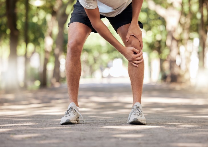 A man holding his knee after suffering an injury during a run. 