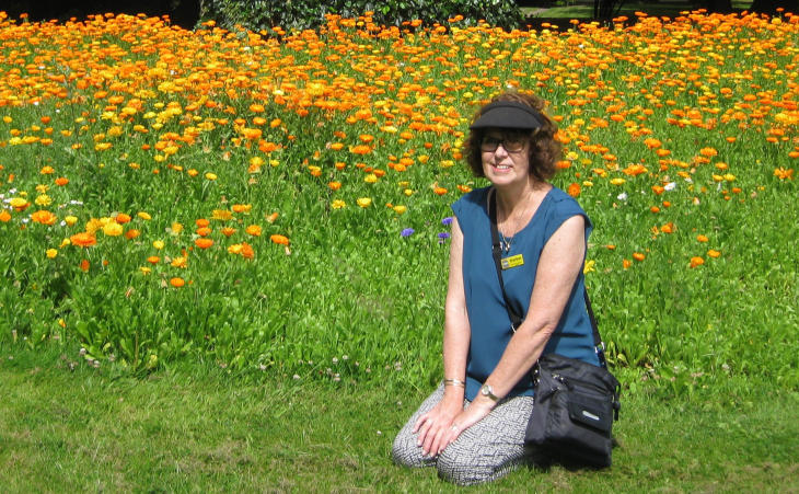 Sharleen Bishop sitting down on her knees with a field of yellow flowers behind her.