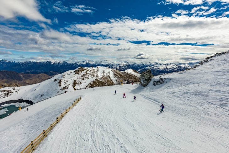 A wide-angle photo of a group of people skiing down a mountain. 