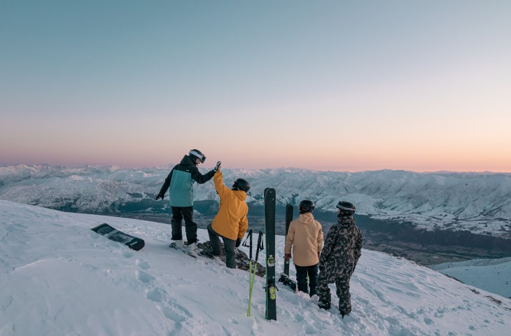Several snowboarders standing on the top of a mountain.