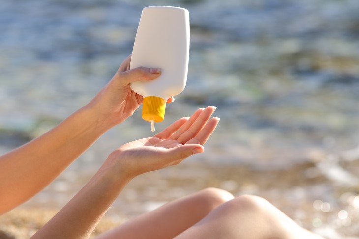 A close-up of a woman squeezing sunscreen out of a bottle onto her hand.