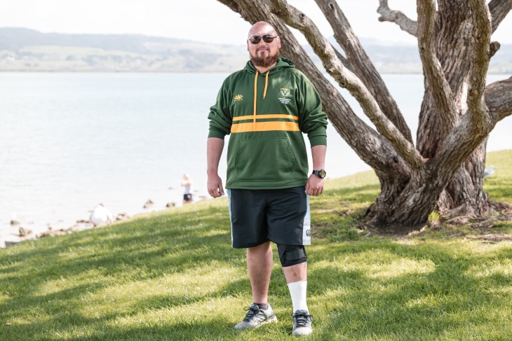 Taane Karena standing on the grass in front of a rural harbour.