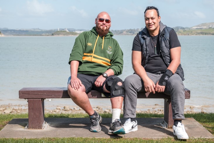 Taane Karena sitting on a bench on the coast with his ACC recovery partner Lance Kilgour.