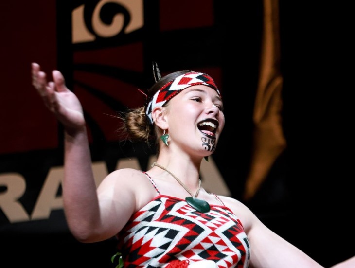 A young woman wearing traditional Māori clothing performing in a kapa haka group.