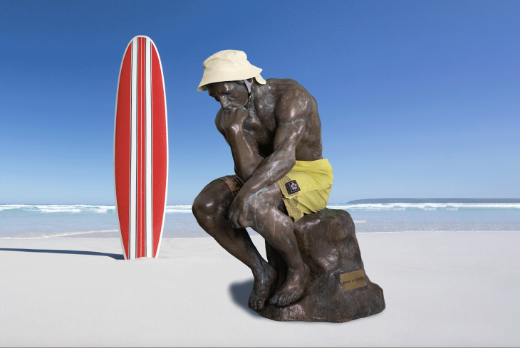 An edited image of 'The Thinker' statue on the beach with a surfboard in the background. 