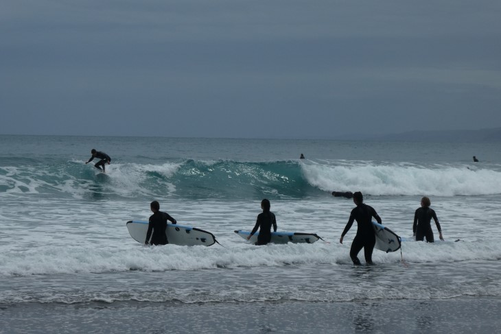 Several surfers walking into the ocean to go surfing.