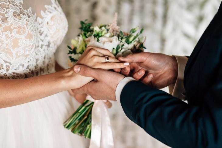 A close-up of a bride and groom's hands showing the wedding ring.