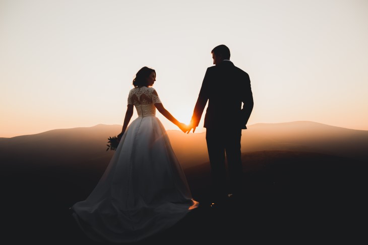 A bride and groom pose in front of a sunset. 