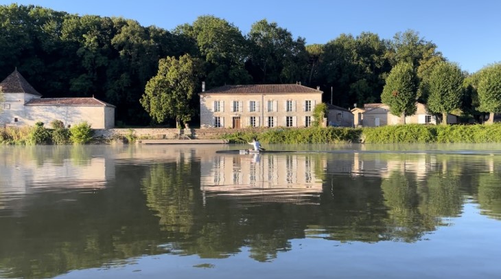 Scott Martlew paddling across a lake in front of several historic buildings while training in Europe.